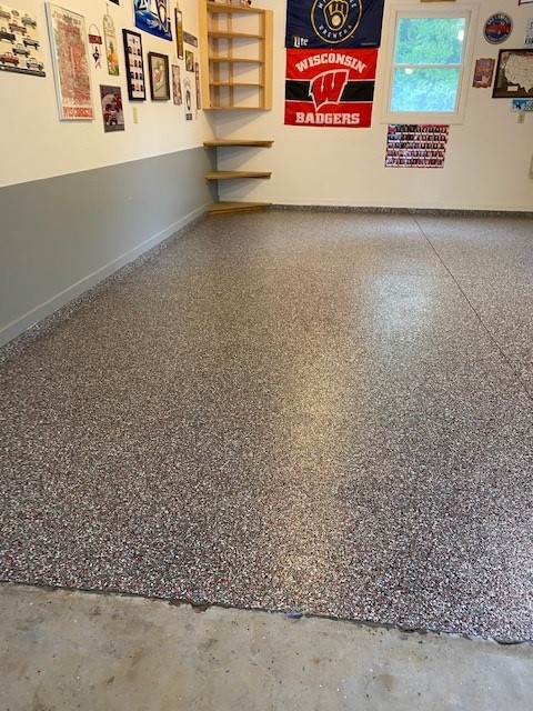 A clean garage with speckled flooring, shelves, and sports memorabilia on the walls. Brightly lit with a window on the side.